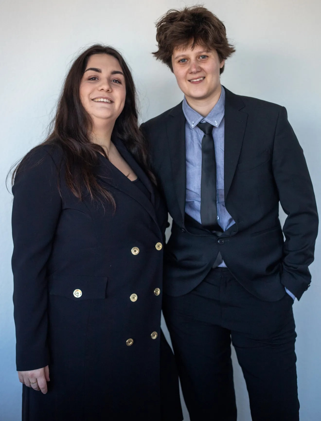 Shannon staat vooraan en Alex achter haar, professioneel gekleed en lachend naar de camera.